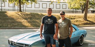 Two Men Standing on a Road in Front of a 1968 Blue Chevy Camaro