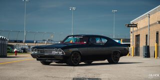 Three Quarters View of a 1969 Black Chevy Chevelle on Empty Ground with a Building Behind It