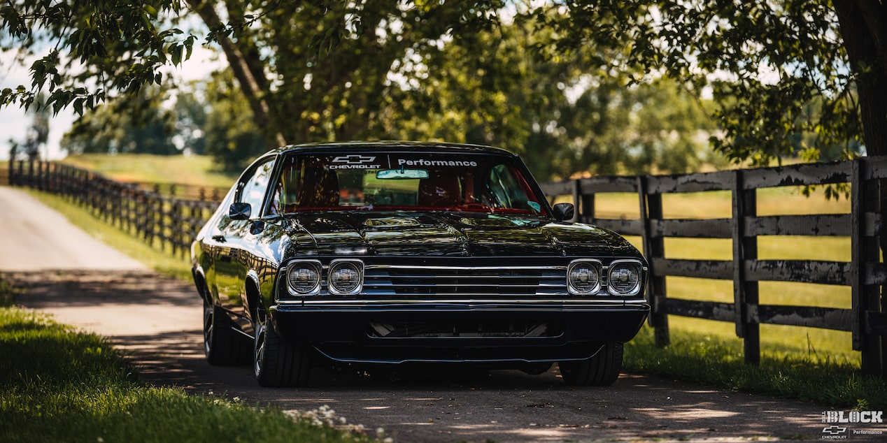 Three Quarters View of a 1969 Black Chevy Chevelle Parked Under Shade Surrounded by Grass and Trees
