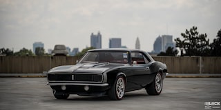 Three Quarters View of a Black 1968 Chevy Camaro Parked on Empty Ground with Buildings in the Distance