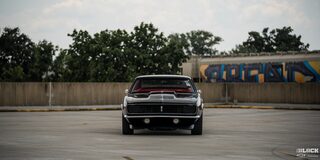 Front Eye-level View of a Black 1968 Chevy Camaro in an Empty Lot Surrounded by a Wooden Fence