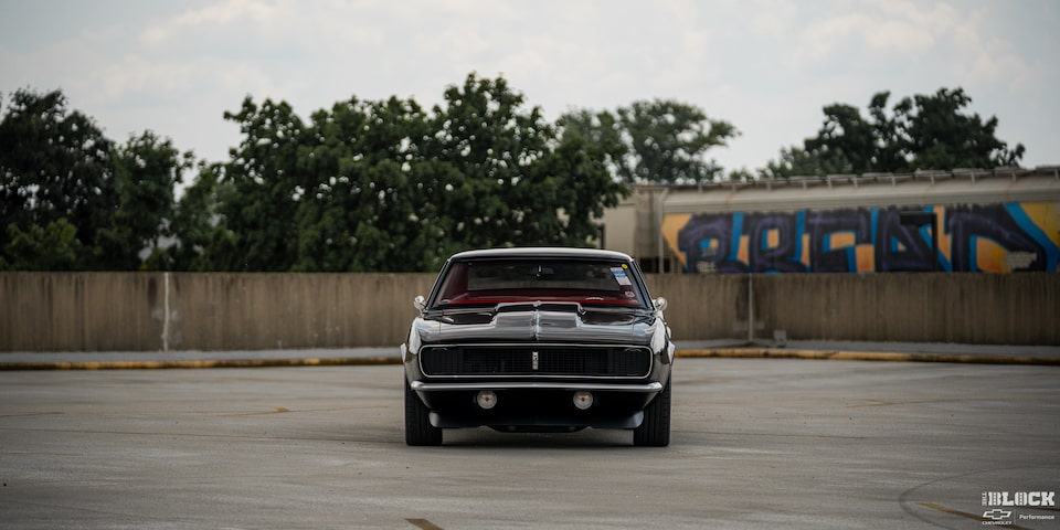 Front Eye-level View of a Black 1968 Chevy Camaro in an Empty Lot Surrounded by a Wooden Fence