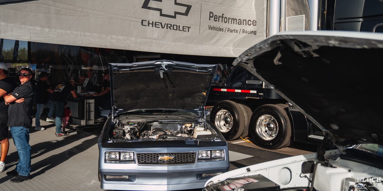 A View of a Chevy Vehicle with Its Hood Open and a Truck Next to It at a Chevrolet Performance Parts Tent
