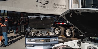 A View of a Chevy Vehicle with Its Hood Open and a Truck Next to It at a Chevrolet Performance Parts Tent
