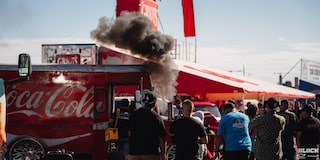 A Crowed of People Standing Next to a Coca Cola Truck and Looking at Smoke Coming Out of a Vehicle