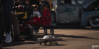 A Tiny Chevrolet Vehicle Toy on the Road with People Seen in the Background