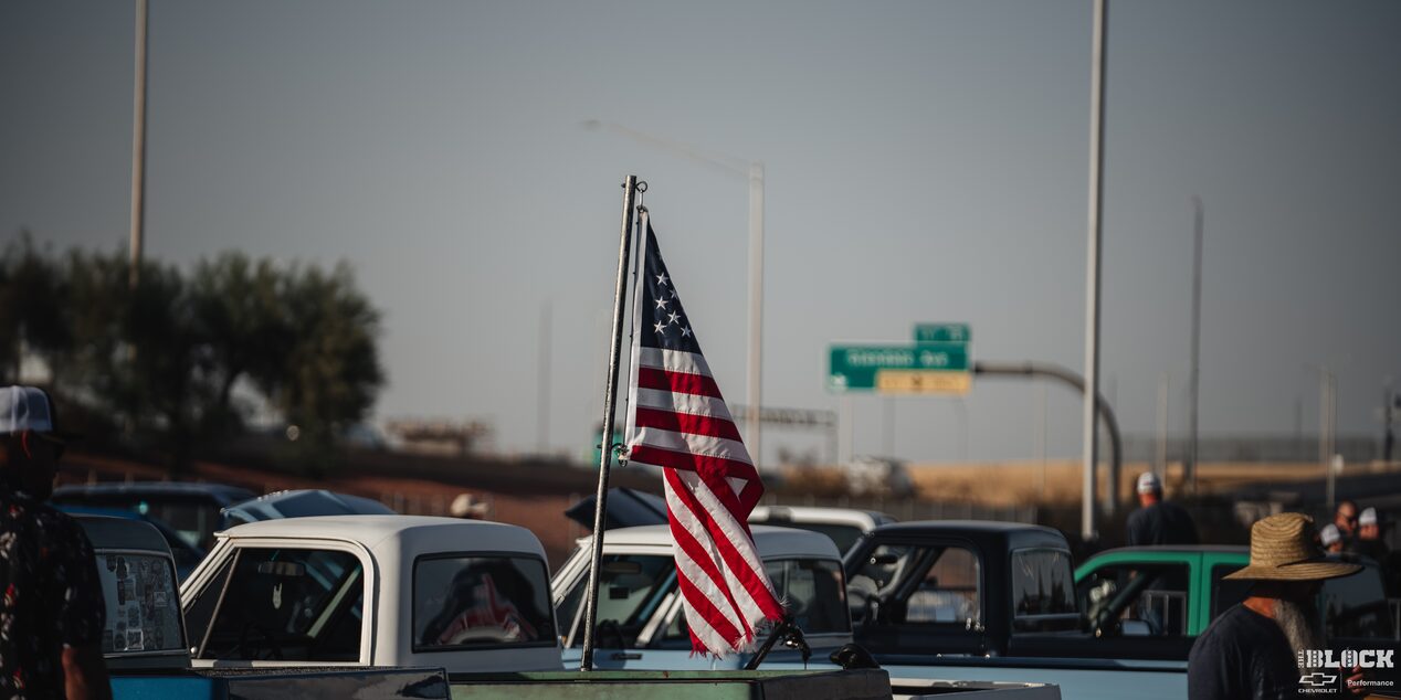 A Shot of the American Flag on Top of a Chevy Pickup Truck with Rows of Trucks Next to It