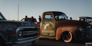 Three Quarters View of a Rusty Pickup Truck Getting Hit by Afternoon Sunlight with Other Pickup Trucks Next to It