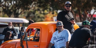 A Couple of Men Wearing Caps Sitting and Leaning on Top of an Orange Pickup Truck