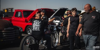 A Couple of Men Walking around and Talking with a Line of Cars with Their Hood Open Seen in the Distance