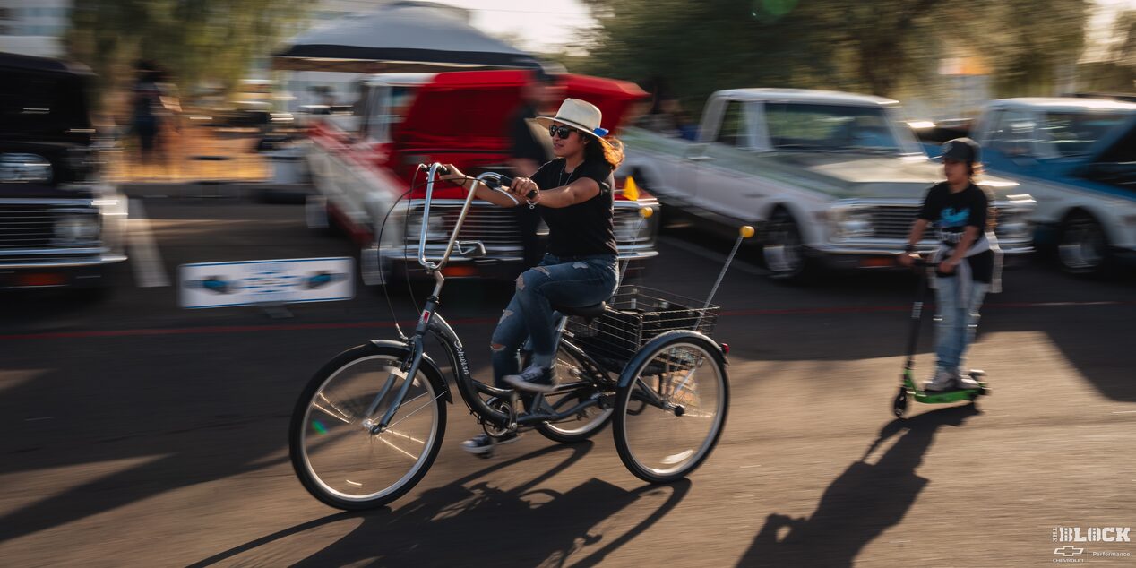 Side View of a Woman Riding a Tricycle with a Boy Riding a Scooter in behind Her