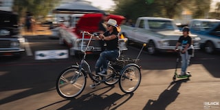 Side View of a Woman Riding a Tricycle with a Boy Riding a Scooter in behind Her