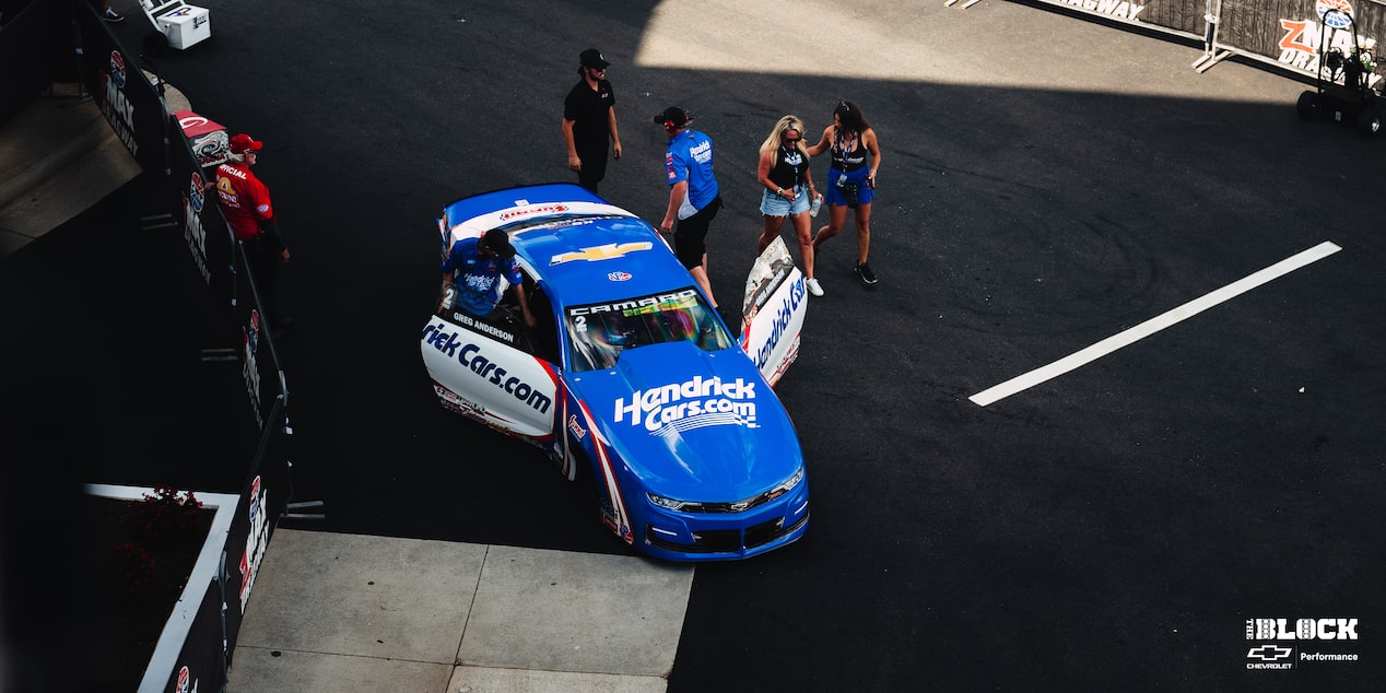 Overhead View of a Blue Chevy Racecar with Its Doors Open and a Man Stepping Out a Couple of People around It