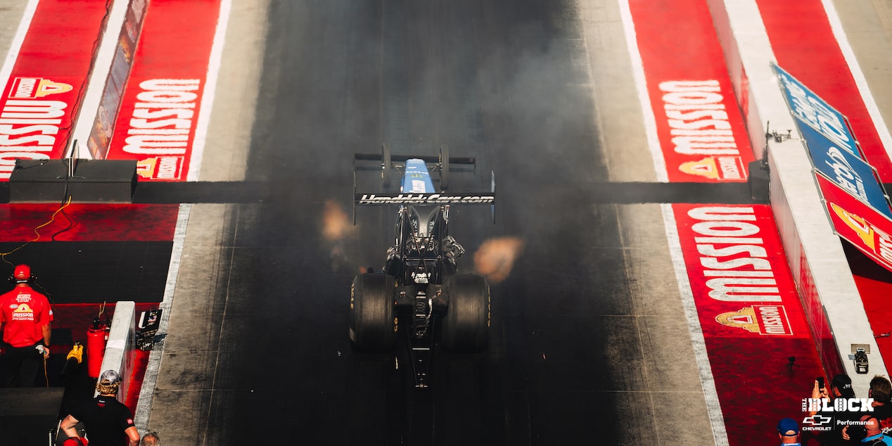 Overhead Shot of a Black Drag Racing Car Going down the Track with Fumes Coming from the Side