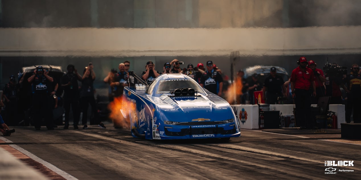 Three Quarters View of a Chevy Blue Racecar Accelerating on a Track with Fumes Coming from the Sides