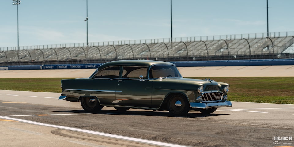 Three Quarters View of a Dark Green 1955 Chevrolet on a Racetrack on a Sunny Day