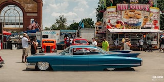 Vista lateral de un auto Chevy clásico de color azul estacionado en frente de un puesto de comida en Goodguys Summit Racing Nationals