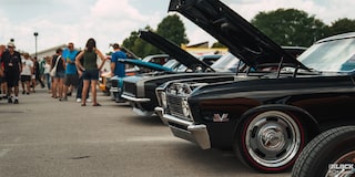 Una gama de autos Chevy clásicos con el cofre abierto en pantalla con gente mirando en los Summit Racing Nationals.