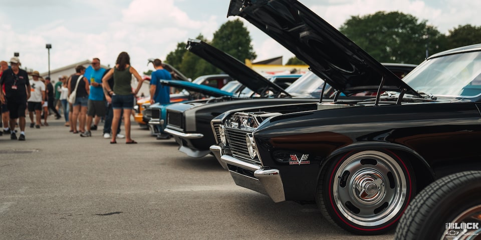Una gama de autos Chevy clásicos con el cofre abierto en pantalla con gente mirando en los Summit Racing Nationals.