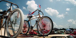 Una bicicleta de época montada en un auto Chevy con una bandera de EE. UU. colocada en el manubrio en los Summit Racing Nationals