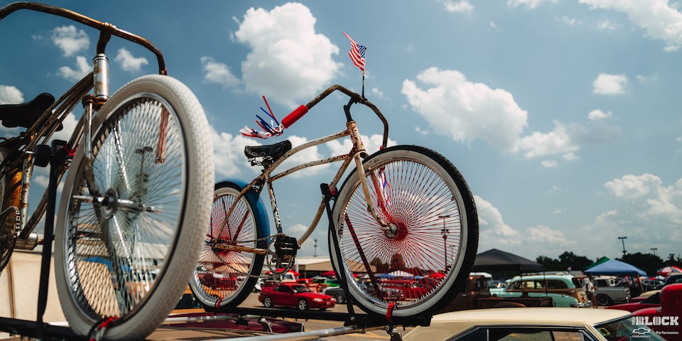 Una bicicleta de época montada en un auto Chevy con una bandera de EE. UU. colocada en el manubrio en los Summit Racing Nationals
