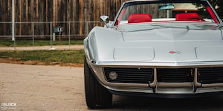 Front View of a 1969 Silver Chevy Corvette Placed to the Left Side of the Frame with a Fence Visible in the Background