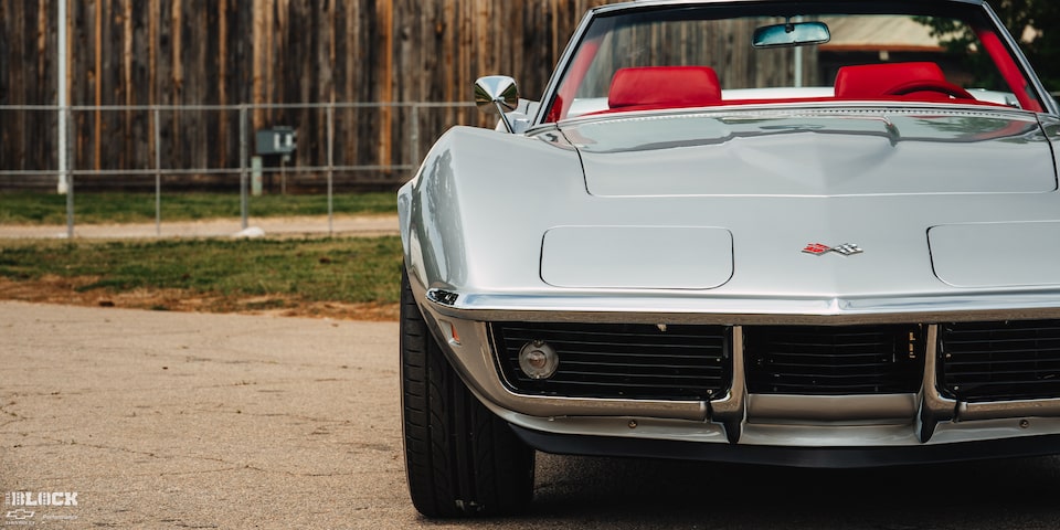 Front View of a 1969 Silver Chevy Corvette Placed to the Left Side of the Frame with a Fence Visible in the Background