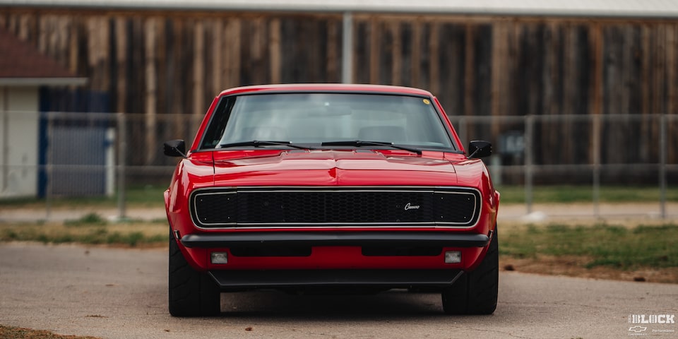 Front Eye Level View of a 1968 Orange Chevy Camaro in Front of a Fence