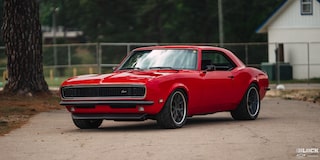 Three Quarters View of a 1968 Orange Chevy Camaro on a Road with a House Behind It