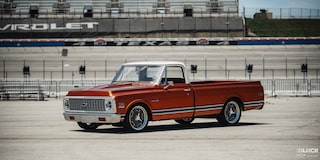 Vista de tres cuartos de una pickup Chevy C10 Naranja en un terreno vacío