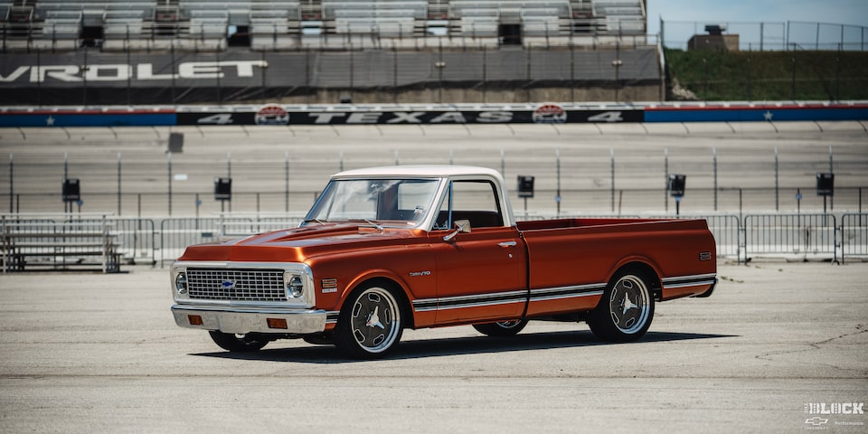 Vista de tres cuartos de una pickup Chevy C10 Naranja en un terreno vacío