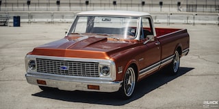 Vista de tres cuartos de una pickup Chevy C10 Naranja en un terreno vacío
