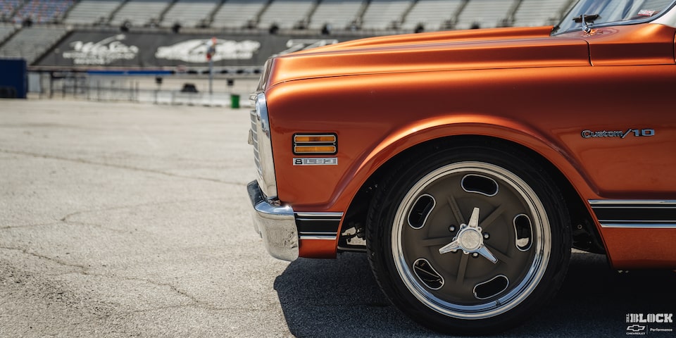 Vista frontal izquierda de una pickup Chevy C10 Naranja con un estadio en la distancia
