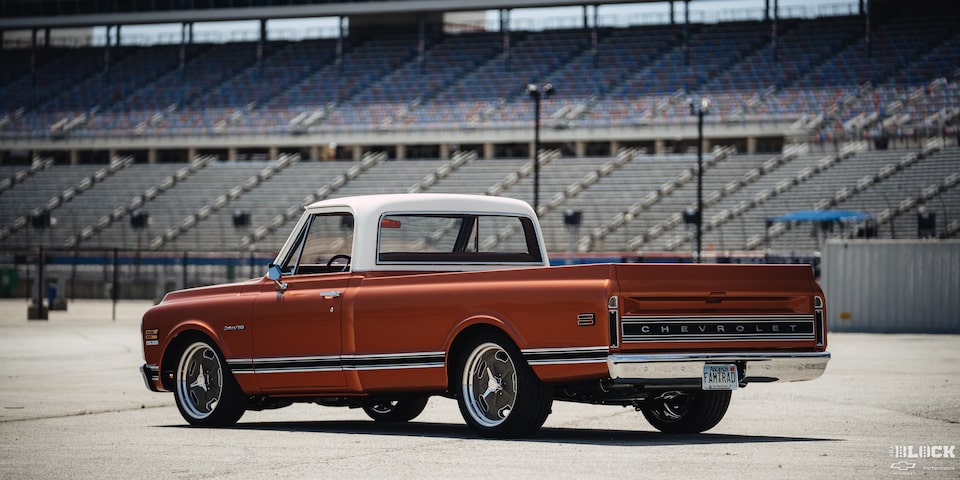 Vista trasera de tres cuartos de una pickup Chevy C10 Naranja frente a un estadio