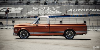 Vista lateral de una pickup Chevy C10 junto a un estadio en la distancia