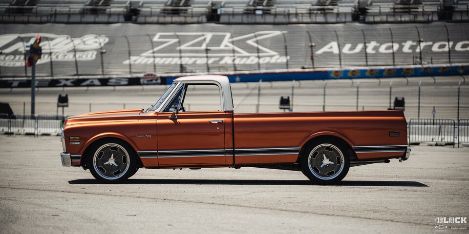 Vista lateral de una pickup Chevy C10 junto a un estadio en la distancia