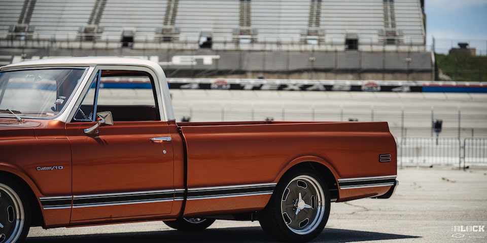 Vista lateral angular de una pickup Chevy C10 junto a un estadio en la distancia