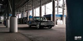 Una Chevrolet C10 1967 en Negro con un motor armado L8P, estacionada debajo de las gradas en una pista de carreras