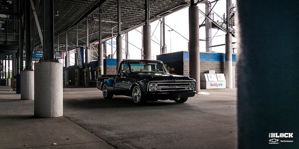 Una Chevrolet C10 1967 en Negro con un motor armado L8P, estacionada debajo de las gradas en una pista de carreras