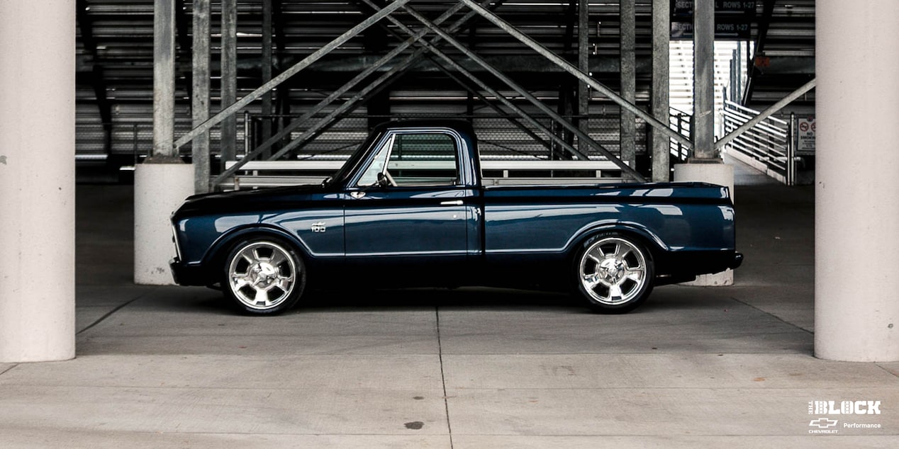 Vista lateral de una Chevrolet C10 1967 en Negro con un motor armado L8P, estacionada debajo de las gradas en una pista de carreras