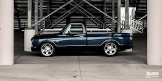 Vista lateral de una Chevrolet C10 1967 en Negro con un motor armado L8P, estacionada debajo de las gradas en una pista de carreras