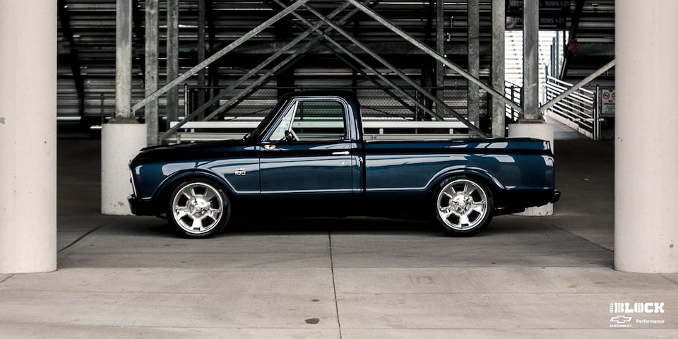 Vista lateral de una Chevrolet C10 1967 en Negro con un motor armado L8P, estacionada debajo de las gradas en una pista de carreras