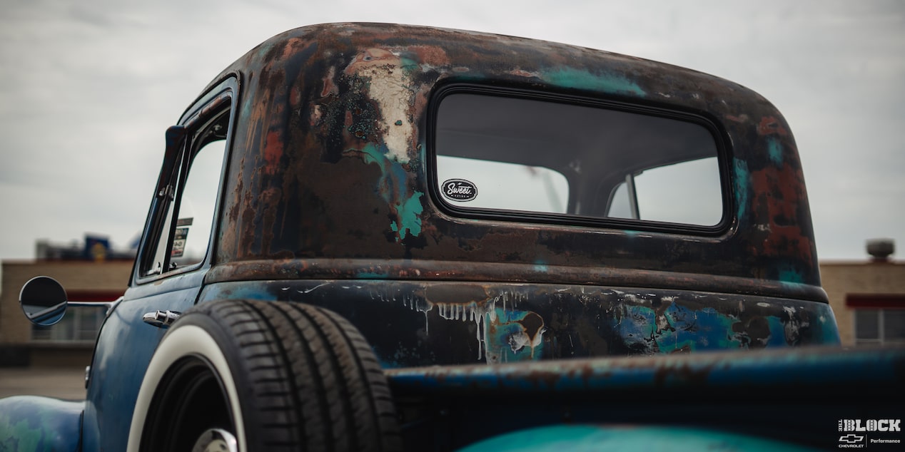 The Back Cab of a Rusty and Discolored 1955 Chevy Pickup Truck under a Cloudy Sky