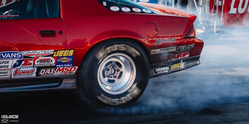 Rear Side View of a Red Chevrolet Sports Car Burning Rubber at the 2024 NHRA 4-Wide Nationals