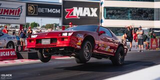 A Red Chevrolet Camaro With Front Wheels Suspended Dramatically in the Air as it Drives the Track at the 2024 NHRA 4-Wide Nationals