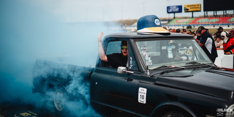 A Black Chevy Pickup Truck Burns Rubber With the Passenger Smiling and Extending His Arm out the Window 