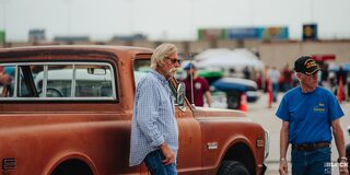 Two Attendees of the 2024 Texas C10 Nationals Stand Outside an Orange Classic Chevrolet Truck