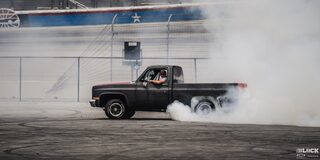 Side View of a Black Chevy Pickup Truck Burning Rubber as the Driver Looks Towards the Camera