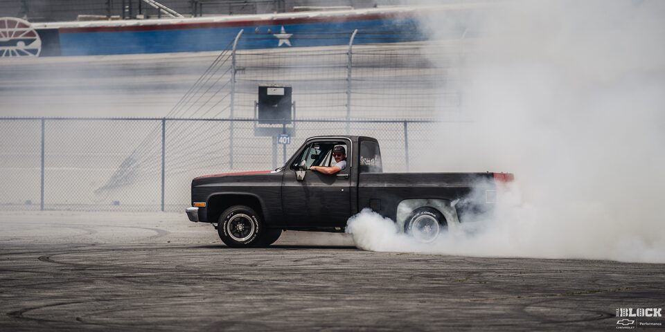 Side View of a Black Chevy Pickup Truck Burning Rubber as the Driver Looks Towards the Camera