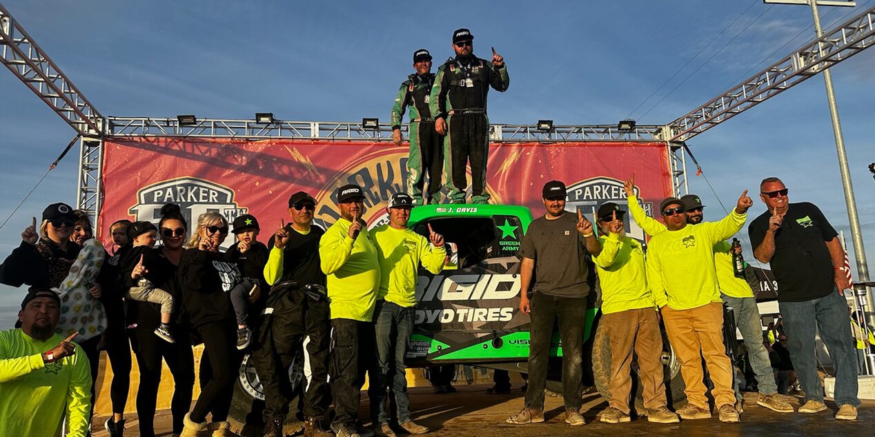 A Group Photo Taken in the Afternoon with Everyone Raising Their Index Finger with Two Men on Top of a Vehicle